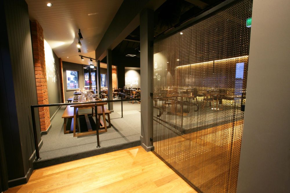 Bronze aluminium chain screen dividing a restaurant entrance from the dining area