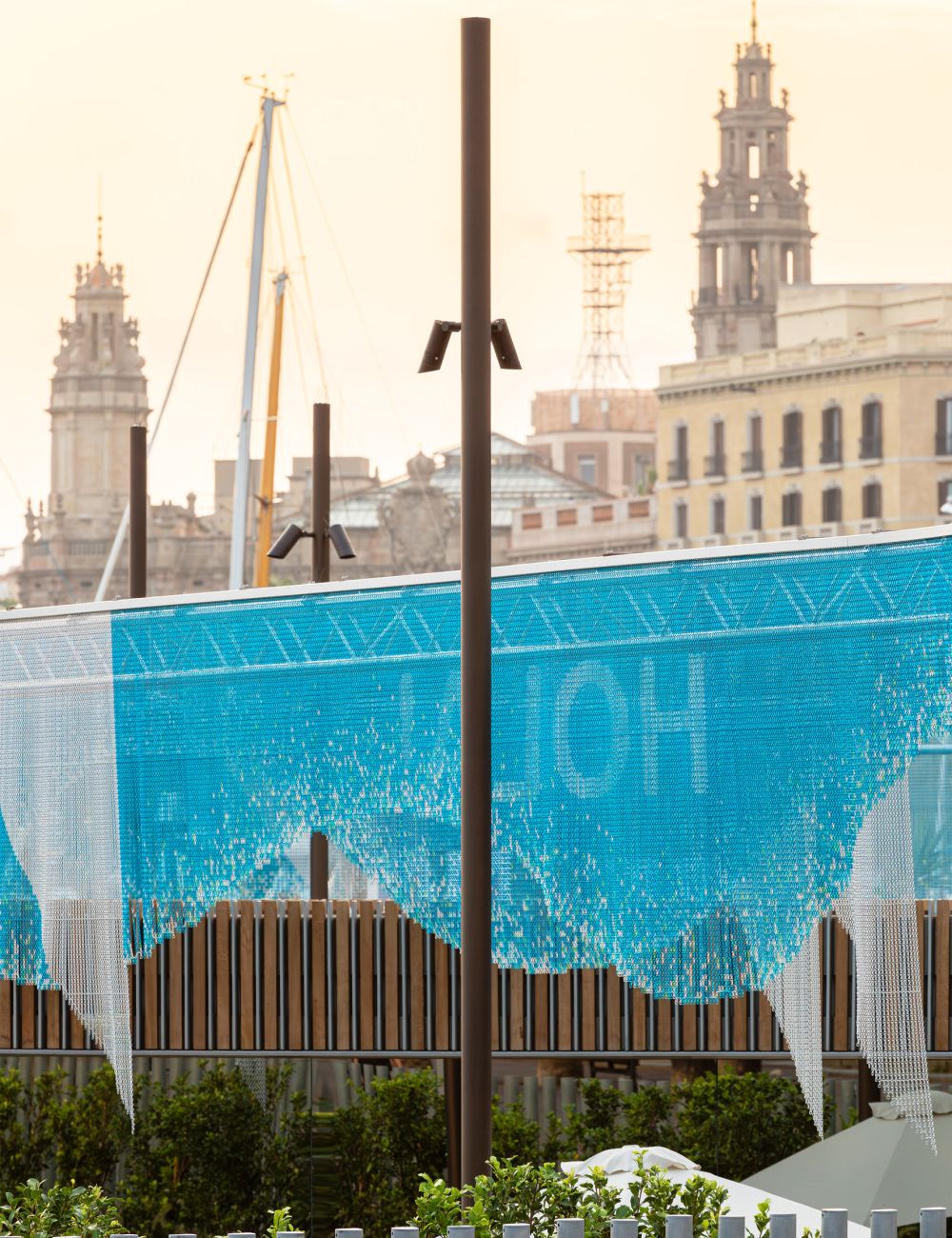 Blue aluminium chain screen installation on a building facade overlooking a city harbour