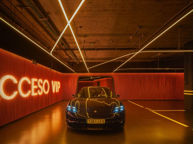 Black sports car in a VIP parking display with an aluminium chain feature wall and dramatic orange lighting